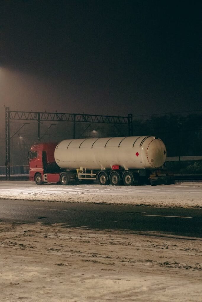 Red truck with tanker parked on snowy road at night in Bydgoszcz, Poland.